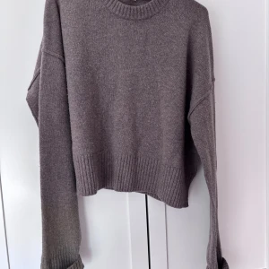 Brun stickad tröja med ribbade detaljer - Mysig brun stickad tröja från arket med breda ribbade muddar och rund halsringning i 100% ull. Tröjan har en loose passform och är lite croppad. Långa ärmar.