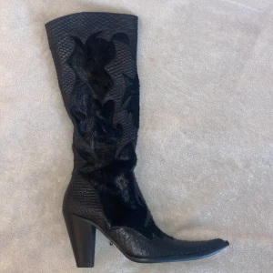 Svarta boots med spetsig tå och klack - Unika svarta boots med spetsig tå och hög klack. Skorna har en cool mix av ormskinnsmönstrat skinn och pälsdetaljer i ett vågigt mönster längs skaftet. Dragkedja på insidan för enkel påtagning. Perfekta för dig som vill sticka ut. Dock är högra skon storlek 37 och vänstra stolek 38 pris kan därför diskuteras. 