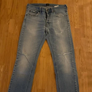 Ljusblå Lee ”Luke” jeans med slitningar - Snygga ljusblå jeans från Lee ”Luke” med klassisk femficksdesign och slitna detaljer vid knäna. Jeansen har raka ben och en normal passform. Perfekta för dig som gillar en avslappnad och trendig look. Materialet är mjukt denim i bomull.
