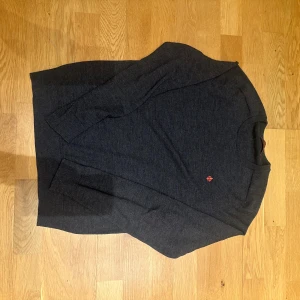 Mörkgrå merinoullströja från Morris - Snygg mörkgrå stickad tröja från Morris i 100% merinoull. Klassisk modell med rund halsringning och diskret röd logga broderad på bröstet. 1599 nypris använd 2 gånger. 