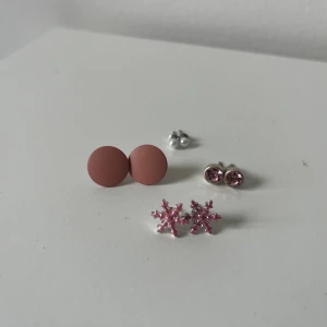 Fyra par örhängen i olika stilar - Säljer fyra par örhängen: ett par runda matta i brunrosa, ett par små silverfärgade pärlor, ett par med rosa glittriga stenar och ett par snöflingeformade i rosa glitter. 