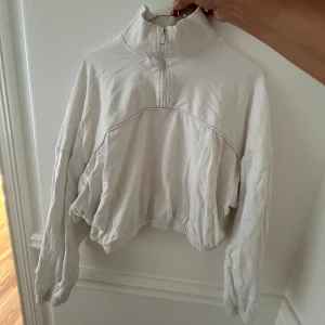 Vit croppad tröja med half zip - Säljer en vit croppad tröja med hög krage och half zip framtill. Tröjan har långa ärmar och elastisk nederkant som ger en snygg, avslappnad passform. 