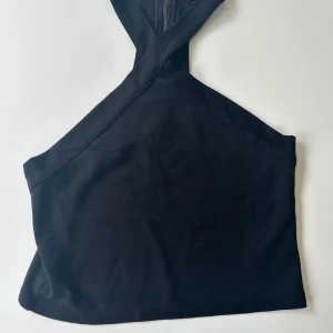 Svart croppad halterneck topp - Säljer en svart croppad topp med halterneck och korsade axelband. Toppen har en stilren och enkel design som passar perfekt till jeans eller kjol. Materialet känns mjukt och bekvämt mot huden.