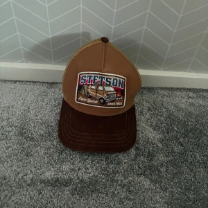 Stetson keps - Säljer en brun och beige truckerkeps från Stetson med broderad patch framtill. Justerbar passform och cool retrostil.