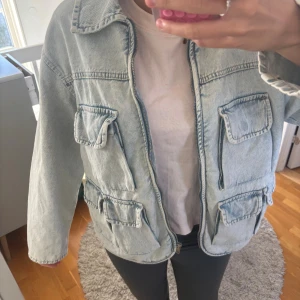 Ljusblå jeansjacka med fickor - Säljer en ljusblå jeansjacka med fyra stora fickor framtill och dragkedja. Jackan har en loose passform och klassisk krage. Perfekt för dig som gillar streetstyle och vill ha en chill look. Materialet är jeans och ärmarna är långärmade.