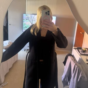 Svart kappa från Pieces - Säljer en svart kappa från Pieces i storlek S. Jackan har lång ärm, knytbälte i midjan och två fickor framtill. Enkel och stilren design som passar perfekt till höst och vinter. Materialet känns mjukt och värmande.