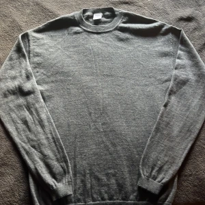 Grå stickad tröja - En enkel och stilren grå stickad tröja. Tröjan har rund halsringning, långa ärmar och ribbade muddar. Perfekt för lager-på-lager och funkar till både jeans och chinos. Materialet är mjukt och skönt, vilket gör den nice för kyligare dagar.