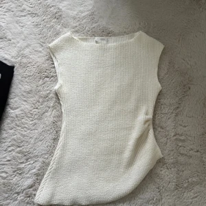 Vit ribbad ärmlös topp från Zara - Säljer en vit ärmlös topp från Zara i storlek M. Toppen har en ribbad struktur och är tillverkad i ett mjukt stickat material. Den har en enkel, rak passform och rund halsringning. Perfekt att styla med jeans eller kjol för en clean look.