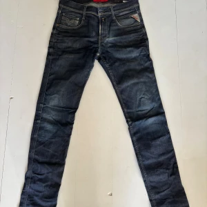 Replay Anbass mörkblå jeans 30/32 - Säljer ett par Replay Anbass jeans i mörkblå tvätt med snygga slitningar och klassiska fem fickor. Jeansen har smal passform och är gjorda i stretchigt denim för extra komfort. Perfekta för dig som gillar en modern och stilren look.