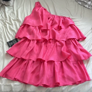 Rosa volang klänning - Supersöt rosa kortklänning från Paul & Joe Sister i 100% silke. Klänningen har flera lager volanger och en snygg oneshoulder-design som ger en cool och trendig vibe. Volangerna ger extra rörelse och flow.