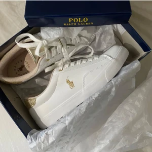 Vita sneakers från Polo Ralph Lauren - Snygga vita sneakers från Polo Ralph Lauren med gulddetaljer och klassisk logga på sidan. Använd cirka 3 gånger. Köpt för 979
