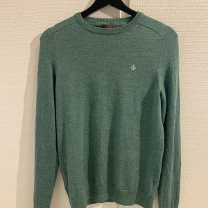 Grön merinoulltröja från Morris - Säljer en stilren grön tröja från Morris i 100% merinoull. Tröjan har en liten broderad detalj på bröstet och ribbade muddar vid ärmslut och nederkant. Perfekt för kyligare dagar!