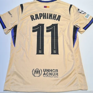 FC Barcelona Raphinha bortatröja Nike - Snygg beige FC Barcelona bortatröja med Raphinha 11 på ryggen. Tröjan har svarta detaljer, klubbmärke, Spotify-logga och Champions League-patch på ärmen. Tillverkad i lätt och ventilerande material, perfekt för match eller supporterliv. Replika, endast handtvätt gäller!