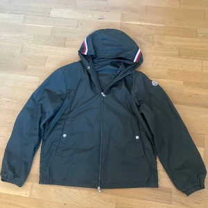 Moncler windbreaker -  100% ÄKTA .Säljer en snygg windbreaker från moncler. Storlek:5 alltså L-xl, Cond 8/10 finns ett litet litet hål i ryggen, bilder kan ordnas! Säljer billigt för att jag inte har nåt behov av den längre(Tar ej byten)