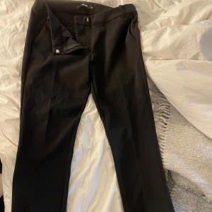 Svarta kostymbyxor från Bik Bok - Snygga svarta kostymbyxor från Bik Bok med klassisk rak passform och pressveck. Byxorna har hällor för bälte, diskreta sidfickor och stängs med dragkedja och hake. Perfekta för en clean och stilren look.