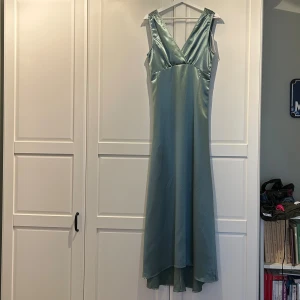 Ljusgrön långklänning  - Snygg ljusgrön långklänning i glansigt satinmaterial med v-ringad omlott överdel och ärmlös design. Perfekt om man ska på bal eller vara brudtärna t.ex. Köpt från vila för ca 2 år sedan men har aldrig kommit till användning (lapp finns fortfarande kvar)! Pris kan diskuteras. Fri frakt 😇
