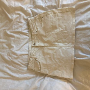 Vit jeanskjol från Weekday - Säljer en snygg vit jeanskjol från Weekday med klassisk femficksdesign och raka linjer. Kjolen är kort och har en stilren look som passar perfekt till sneakers eller boots. Materialet är kraftigt denim och kjolen har knapp- och dragkedjestängning framtill.