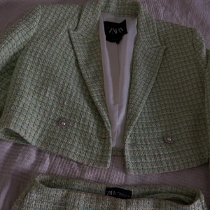 Grön rutig kostym från Zara - Snygg grön rutig kostym från Zara med croppad kavaj och matchande skorts. Kavajen har pärlknappar med silverdetaljer och klassisk krage. Kjolen har coola slitsar framtill. Materialet är tjockt och strukturerat, perfekt för att sticka ut. Endast använd en enstaka gång, i perfekt skick!! Skorts är storlek XS och kavaj storlek S 