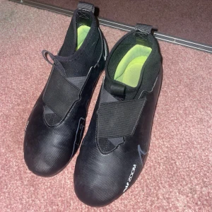 Nike Air Zoom svarta fotbollsskor - Snygga svarta Nike Air Zoom fotbollsskor med grå detaljer och gula dobbar. Skorna har en strömlinjeformad design med elastiskt band över vristen och diskret Nike-logga på sidan. Ovandelen är i syntetmaterial och insidan har en limegrön dämpning för extra komfort.