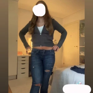 Mörkblå slitna jeans med låg midja - Säljer ett par mörkblå jeans med slitningar på knäna och låret. Jeansen har låg midja och klassisk femficksdesign. Modellen är rak och materialet är stretchigt jeans, vilket gör dem bekväma och snygga till vardags. Perfekta för dig som gillar en avslappnad stil.