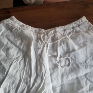 Vita linnebyxor med snörning, M - Luftiga vita linnebyxor med elastisk midja och snörning framtill. Perfekta för varma dagar och chill vibes. Byxorna har en avslappnad passform och är tillverkade i svalt linnematerial. Enkla att matcha med t-shirt eller skjorta.