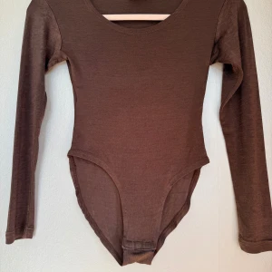 Brun långärmad body från Basic Moderne - Säljer en brun långärmad body från Basic Moderne. Den har rund halsringning och är i ett mjukt, stretchigt material. Perfekt att styla med jeans eller kjol för en clean och enkel look.