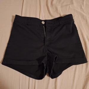 Svarta shorts från H&M Divided - Svarta shorts från H&M Divided i klassisk jeansstil med dragkedja och knapp framtill. Modellen har två bakfickor och uppvikta benslut. Perfekta för sommarens alla häng, snygga till crop top eller hoodie. Materialet ser ut som jeans men är mycket mjukare och stretchingare, vet dock inte vad det är för matreal🫶🏻