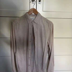 Beige skjorta från East West, stl S - Stilren beige skjorta från East West i storlek S. Skjortan har klassisk krage, knäppning framtill och långa ärmar med manschett. Perfekt för dig som gillar en enkel och clean look. Materialet känns mjukt och lätt, troligen bomull eller linne. Skjortan är använd 1 gång och skicket är 10/10. 