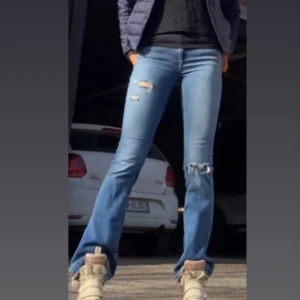 Blå bootcut jeans med slitningar - Säljer ett par mid waist blå bootcut jeans med slitna detaljer vid knäna och råa, innerbenslängd 83cm💕