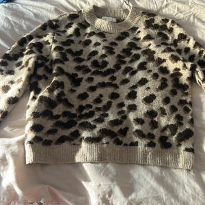 Beige leopardmönstrad stickad tröja H&M - Supermysig stickad tröja från H&M i beige med leopardmönster i brunt och svart. Tröjan har rund halsringning, ribbade muddar och lång ärm. Perfekt för dig som vill sticka ut lite extra i höst och vinter!