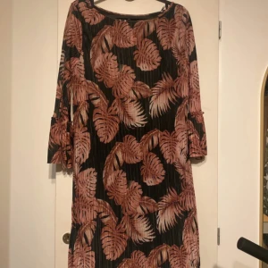 Söt klänning vila💗 - Svart klänning från Vila med rosa-bruna bladmönster och trekvartsärmar. Klänningen har en rak passform och är tillverkad i ett lätt, plisserat material som ger en snygg struktur. Perfekt för dig som gillar trendiga prints och bekväma snitt.