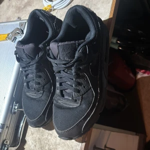 Svarta Nike Air Max sneakers - Svarta Nike Air Max sneakers med klassisk siluett och tydlig Nike Air-logga på hälen. Skorna har snörning, mesh och syntetmaterial på ovandelen samt platt sula. Perfekta för dig som gillar en sportig och stilren look.