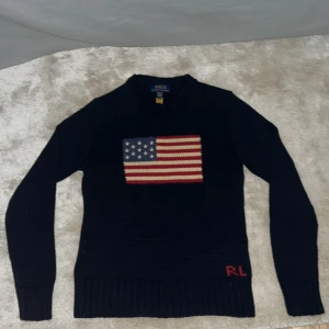 Mörkblå stickad tröja Polo Ralph Lauren - Mörkblå stickad tröja från Polo Ralph Lauren med amerikansk flagga framtill och RL-broderi i rött nedtill. Perfekt för dig som gillar grisch stil. Har aldrig använts pga fel storlek och pris kan diskuteras!