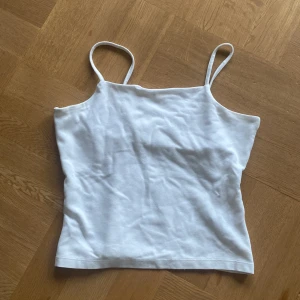 Vit linnetopp från Lindex - Säljer en enkel och fräsch vit linnetopp från Lindex med smala axelband. Toppen är rak i modellen och tillverkad i mjuk bomull, perfekt för varma dagar. Stilren och lätt att matcha med allt. Passar dig som gillar minimalistisk stil. 