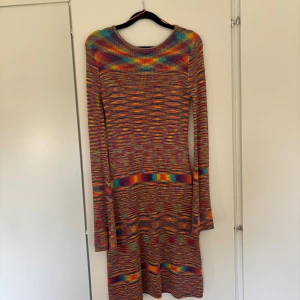 Färgglad stickad långärmad klänning - Säljer en unik och färgglad stickad klänning med lång ärm och rund hals. Klänningen har ett coolt mönster i rött, gult, blått och grönt som ger den en riktigt vibey look. Perfekt för dig som vill sticka ut med en bekväm och mjuk outfit. Även öppen i ryggen