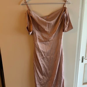 Champagnefärgad långklänning Oh Polly - Säljer en elegant långklänning från Oh Polly i champagnefärgad satin. Klänningen har offshoulder-design med draperad halsringning och smala axelband. Materialet är glansigt och mjukt, vilket ger en lyxig känsla. Perfekt för dig som vill sticka ut med stil.