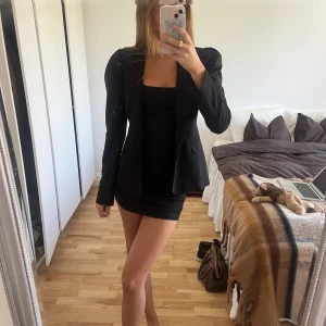 Svart fitted kavaj från NAKD med puffärm - Snygg svart kavaj från NAKD med puffade axlar och klassisk krage. Kavajen har två knappar framtill och fickor med lock. Materialet är mjukt och känns som polyester, perfekt för en stilren look. Passformen är normal och axlarna ger en cool feminin siluett.