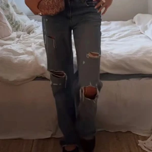 Populära Blå slitna wide jeans från Zara - Snygga blå jeans med slitningar och hål på benen. Modellen är wide fit med raka ben och klassisk femficksdesign. Perfekta för en avslappnad och trendig look.