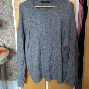 Grå kabelstickad tröja från BikBok - Mysig grå kabelstickad tröja från BikBok i storlek L. Tröjan har rund halsringning, lång ärm och ett klassiskt stickat mönster som ger en chill och stilren vibe. Perfekt att slänga på sig när det är kallt ute.