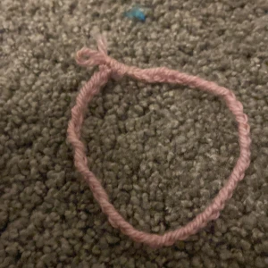 Rosa handgjort garnarmband - Säljer ett enkelt och charmigt armband gjort av rosa garn. Perfekt för dig som gillar unika och handgjorda accessoarer. 