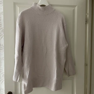 Ljusbeige stickad polotröja - Mysig och oversized stickad polotröja i ljusbeige färg. Tröjan har ribbade muddar vid ärmslut, nederkant och hals, samt lång ärm och hög krage. Perfekt för lager-på-lager och chill dagar.