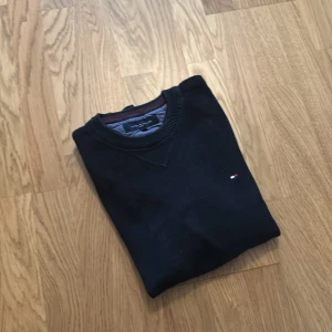 Svart tröja från Tommy Hilfiger Sport - Svart långärmad tröja från Tommy Hilfiger Sport med rund halsringning och diskret broderad logga på bröstet. Tröjan har ribbade muddar och krage samt insida i kontrastfärg. Perfekt för en clean och stilren look.