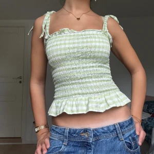 Grön- och vitrandig smockad linnetopp - Supersöt smockad linnetopp i ljusgrönt och vitt med volangkant nertill och knytbara axelband. Toppen har ett randigt mönster och är croppad, perfekt för fest