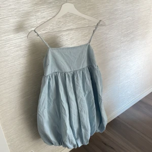 Ljusblå ballongklänning med smala axelband - Superfin ljusblå kortklänning med ballongformad kjol och smala, justerbara axelband. Klänningen har en rynkad detalj i ryggen och är tillverkad i mjuk bomull. Perfekt för dig som gillar en unik och luftig look med volym. (Aldrig använd)