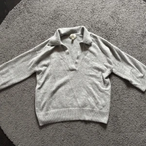 Grå polotröja från H&M med v-ringning - Säljer en stilren grå polotröja från H&M i storlek S. Tröjan har en bred krage och djup v-ringning, samt långa ärmar och ribbad nederkant. Perfekt för dig som gillar enkel och clean look med lite oversized känsla.