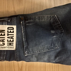 Dsquared2 blå skinny jeans med slitningar - Snygga blå jeans från Dsquared2 med coola slitningar och tvättade detaljer. Modellen är skinny fit med klassiska fem fickor och stor vit patch med Dsquared2-logga bak. Jeansen har en mörkblå bas med ljusare partier och distressed look.