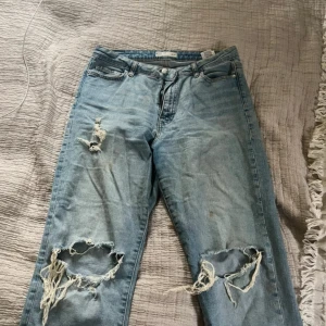Ljusblå ripped jeans - Säljer ett par ljusblå jeans med stora slitningar och hål på båda knäna. Modellen är rak och midjehög. Köpte från Gina tricot 