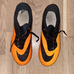 Nike Hypervenom fotbollsskor orange/svart - Säljer ett par Nike Hypervenom fotbollsskor i storlek 38. Skorna är i en cool orange och svart färg med stora Nike-loggor och mönstrad ovandel. De har snörning och fasta dobbar för gräsplan. Perfekta för dig som vill sticka ut på planen!