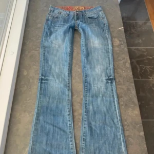Blåa jeans från JC Jeans med brodyr - Snygga ljusblå jeans från JC Jeans med klassisk femficksmodell och orange broderi på bakfickorna. Byxorna har låg midja och bootcut-ben, samt ett färgglatt innerfoder i midjan. Perfekta för dig som gillar en avslappnad och trendig look. Midja - 38 höjd- 18 innerben - 84