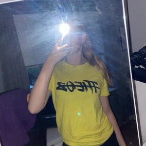 Gul THEOZ t-shirt med tryck - Gul t-shirt med svart THEOZ-tryck på bröstet. Använd på någon koncern när jag va yngre men kommer aldrig till användning längre, superskönt material. 